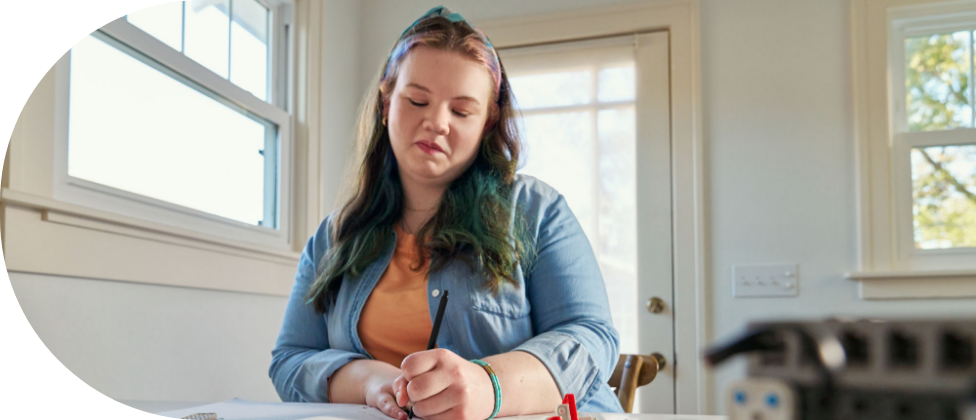 A young woman sitting at a table writing a note.