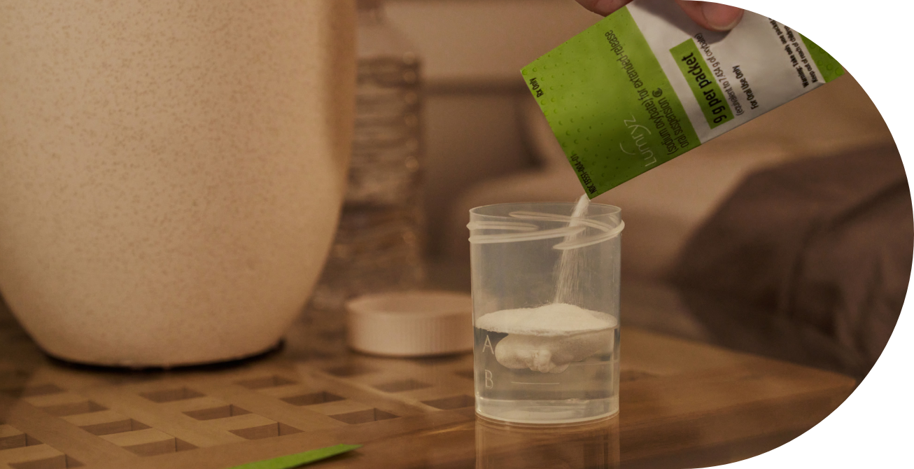A photograph of a hand pouring a premeasured packet of LUMRY into a glass of water