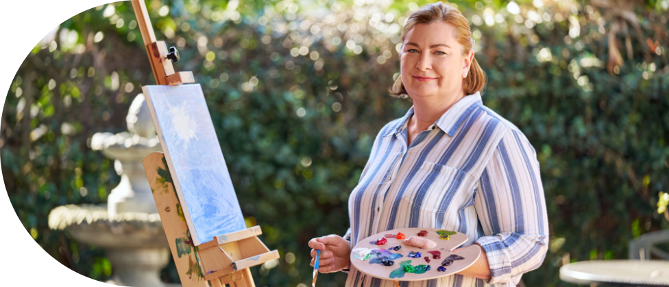 A woman holding a paintbrush and palette, standing in front of an easel.